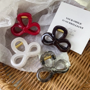 Elegant bow-shaped hair claws in four colors displayed in a rustic woven basket