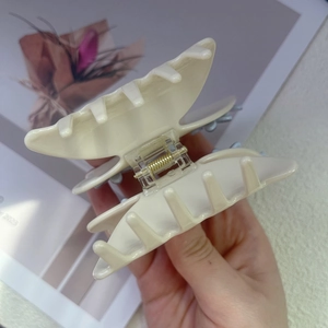Macro view of ivory hair claw clip showing golden metal spring and interlocking teeth detail