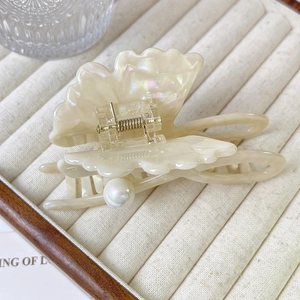 Détail d'une pince à cheveux papillon nacrée avec perle sur un plateau beige élégant