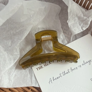Detail of translucent olive green hair claw clip with golden metal spring on white paper