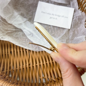 Detail of cream white resin hair clip showing gold metal base and clamp mechanism