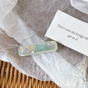 Close-up of marble acetate hair clip in mint green and cream on a decorative background