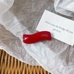 Close-up of a glossy red wavy hair clip with golden France Handmade lettering on it