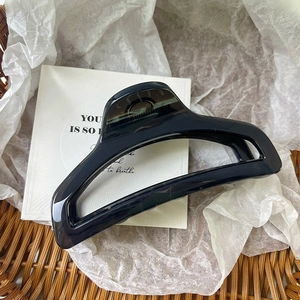 Dettaglio di una pinza per capelli geometrica nera in resina su uno sfondo minimalista