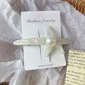 Détail d'une barrette étoile de mer en acétate avec perle sur sa carte de présentation
