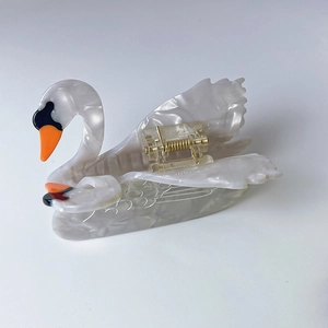 Gros plan d'une pince à cheveux cygne en acétate avec texture nacrée blanche et ressort doré