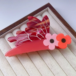 Detail of red marble acetate butterfly hair clip with floral accents on jewelry box