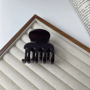 Detail of glossy deep purple claw clip on beige velvet tray with elegant styling