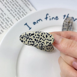 Elegant acetate hair clip with cream and black dalmatian pattern held in hand