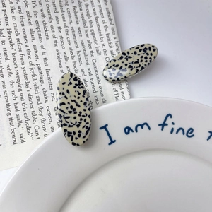 Close-up of two acetate hair clips with black and white spotted texture on newspaper