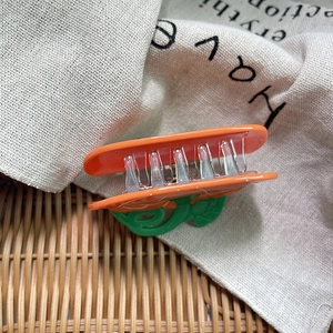 Détail d'une pince à cheveux orange en forme de carotte avec feuilles vertes sur tissu