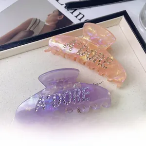 Detail of acetate shark hair clips with A'DORE rhinestone lettering on marble texture