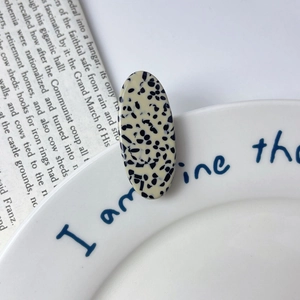 Macro detail of oval acetate hair clip featuring cream base with black dalmatian spots