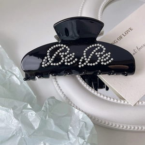 Detail of a black glossy hair claw clip featuring elegant pearl BeBe lettering in cursive
