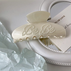 Detailed view of cream acrylic hair claw clip with BeBe pearl lettering and glossy finish
