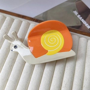 Détail d'une pince à cheveux brillante en forme d'escargot orange et jaune sur plateau