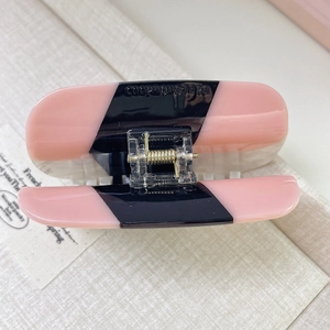 Detail of a pink and black acetate hair claw clip with engraved logo and golden metal spring