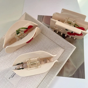 Detailed view of beige acetic acid hair claws featuring red cherry and green leaf patterns