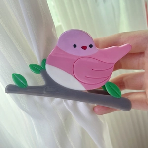 Detailed bird design hair claw clip made of pink and green acetate on a grey branch