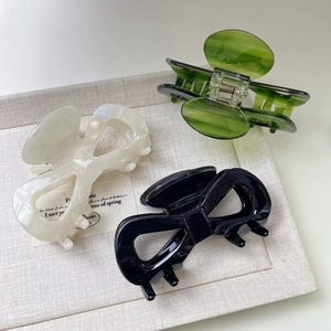 Three elegant acetate bow hair claws in white pearl, black, and marble green colors