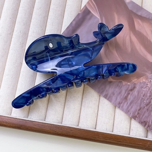 Detailed view of dark blue whale-shaped acetate hair claw clip on soft fabric background