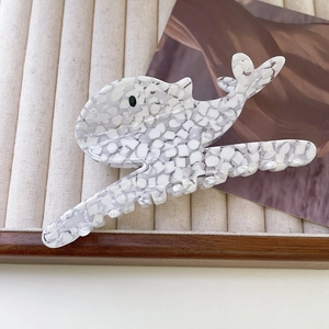 Detail of whale-shaped acetate hair claw clip with marble texture on velvet tray