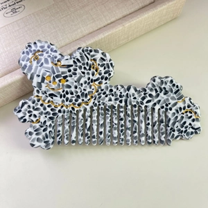Détail d'un peigne en acétate motif vache avec un design doré de visage d'animal