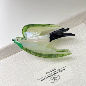 Detail of bird-shaped acetate hair claw clip on linen tray with artistic paper card