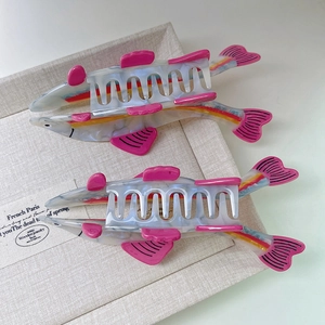 Close-up of shark-shaped acetate hair claws with pearlescent finish and pink fins