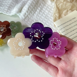 Détail montrant des pinces à cheveux à fleurs avec perles et acétate coloré en main