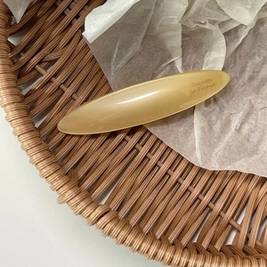 Close-up of champagne leaf oval barrette with Barrette la France text on white tissue