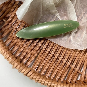 Detail view of the deep olive green oval acetate barrette with golden French lettering