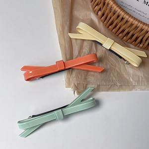 Trois barrettes nœuds colorées en jaune, orange et vert sur un fond rustique minimaliste