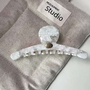 Détail macro d'une pince à cheveux en acétate avec logo doré sur pochette en toile
