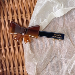 Detail of a vintage bow hair clip in amber brown featuring a gold 'La France' logo
