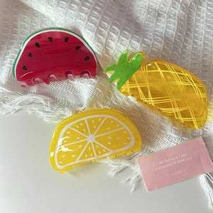Three acrylic hair claws in watermelon, pineapple and lemon shapes on white fabric