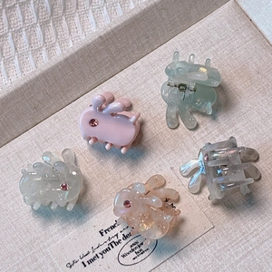 Five colorful cute bunny hair claws with rhinestones on a beige textured display tray