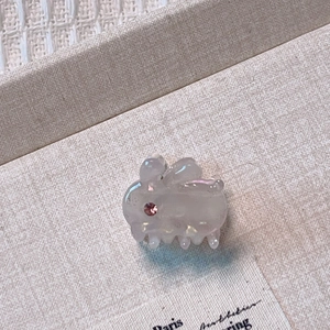 Close-up of a pearlescent white bunny hair claw clip with a sparkling red rhinestone eye