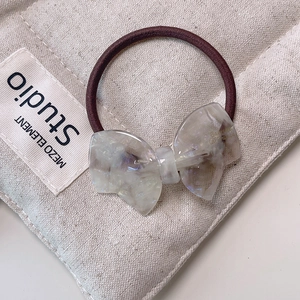 Macro detail of a translucent acetate bow hair tie with golden French lettering