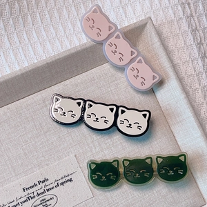 Détail de trois barrettes chat en acétate rose, blanc et vert sur un plateau tressé