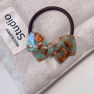 Close-up of light green marbled acetate bow hair tie on a beige canvas background