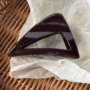 Macro detail of a triangular hollow acrylic hair claw clip on white textured paper