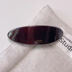 Close-up of a burgundy acetate hair barrette with gold lettering on a canvas bag background