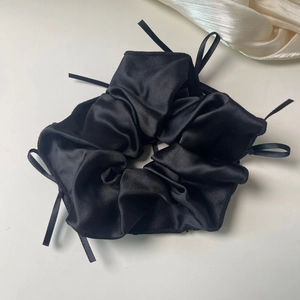 Detail of a black silk scrunchie with delicate ribbon bows on a gray background