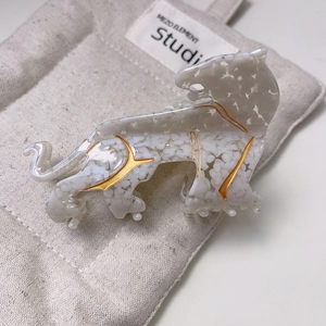 Elegant leopard hair claw clip in white acetate with gold accents on a linen background