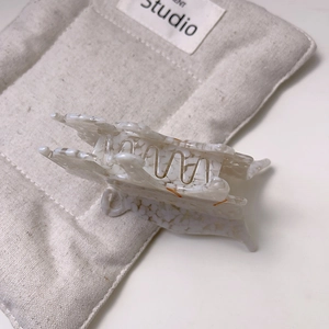 Détail de la pince à cheveux en acétate à motif marbré sur fond de sac matelassé beige