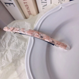 Détail du motif floral à l'intérieur d'une barrette rose en acétate sur un plateau blanc