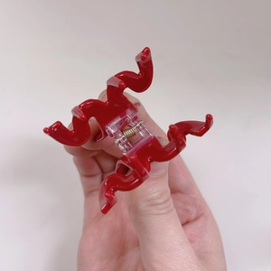 Détail d'une pince à cheveux rouge avec dents ondulées et ressort en métal doré