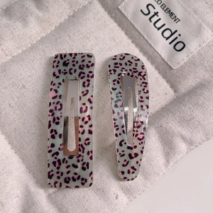 Detail view of two leopard print hair clips in mint green resin on a soft white fabric
