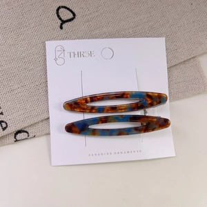 Close-up of tortoise shell acetate hair clips with blue and brown patterns on a white card